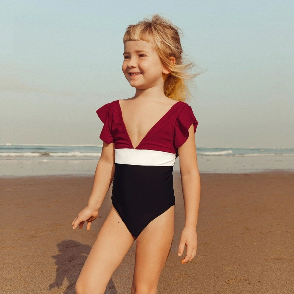 Glimlachend blond meisje op het strand dat een eendelig zwempak draagt