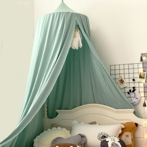 Groen babybedje boven een wit bed met witte, beige en grijze kussens voor een witte muur