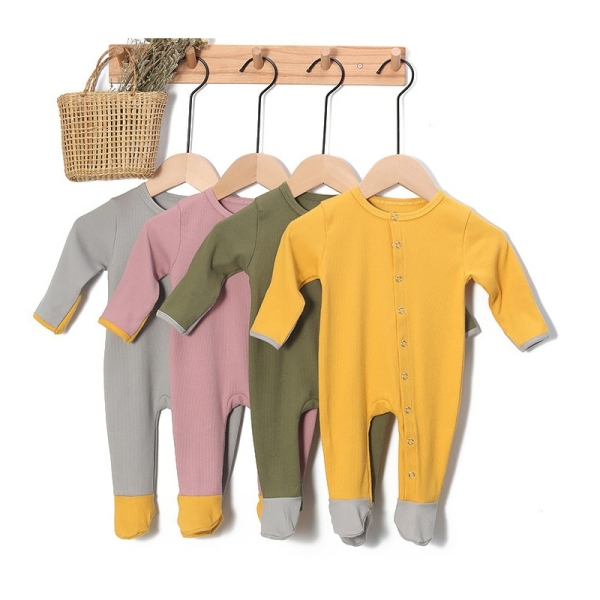 Geribbelde baby romper in geel, groen, roze en grijs katoen hangend aan hangers aan een beige wandkapstok met een rieten mandje