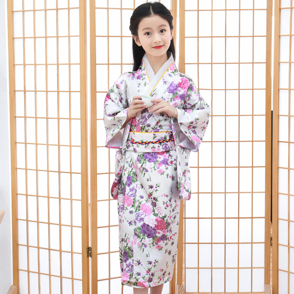 voor een Japans scherm draagt een klein meisje een traditionele witte kimono met een roze bloemmotief