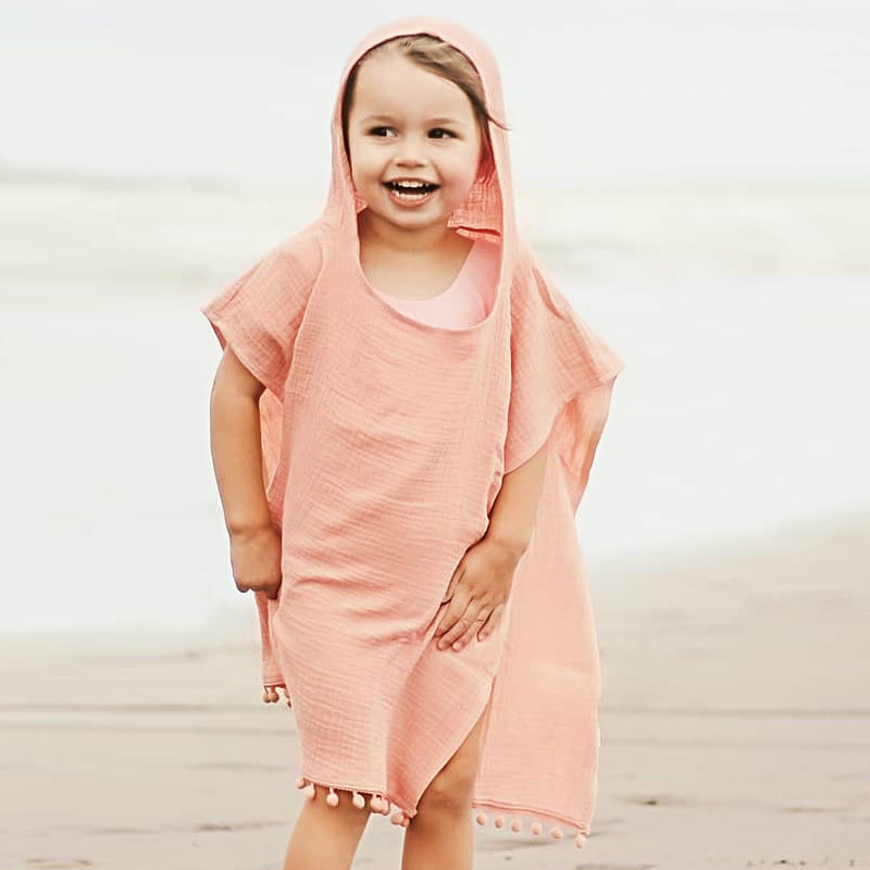 Meisjesstrandkleding met roze kap gedragen door een meisje op het strand