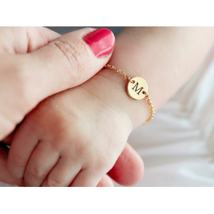 Armband met initialengravure voor babymeisje op de pols van een goudkleurige baby met kettingschakel