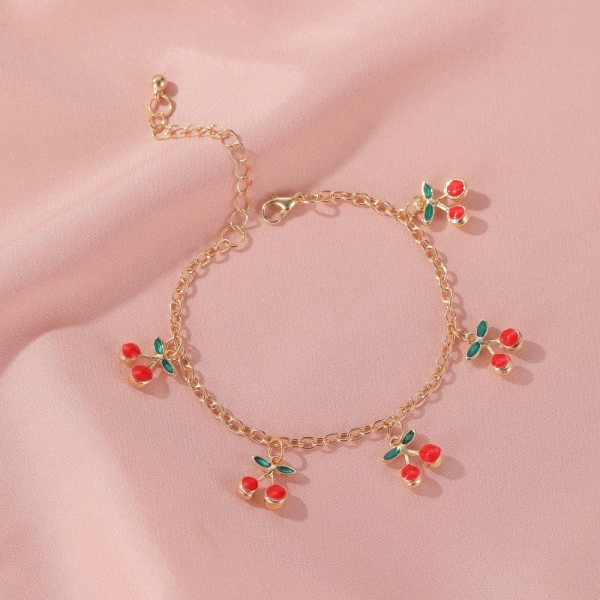 De mesh armband met kersenbedeltje voor babymeisjes is gezet op een roze blad, gemaakt van schakelketting met vijf kleine kersenbedeltjes. Het heeft een warme sluiting