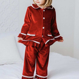 Klein blond staand meisje, draagt rood fluwelen kerstpyjama