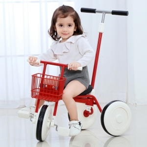 Klein bruin meisje zittend op een rode driewieler in een kamer bij een raam